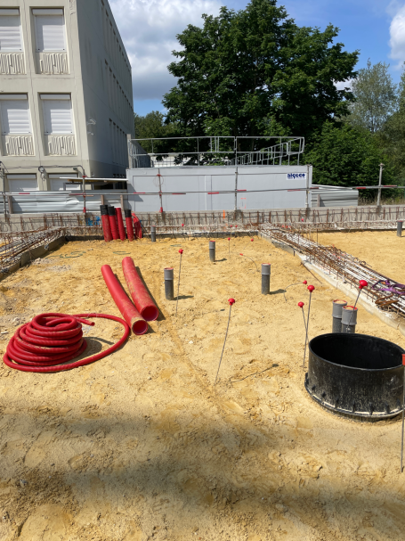 Chantier de construction avec des tuyaux, des fondations en béton et des équipements.