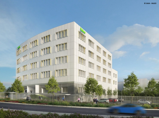 Bâtiment moderne à plusieurs étages avec arbres et route à proximité.