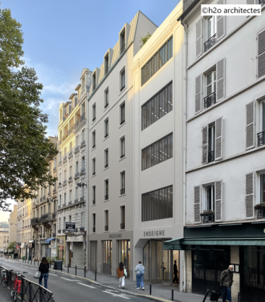 Édifice moderne en béton avec fenêtres, situé dans une rue parisienne, sous un ciel bleu.