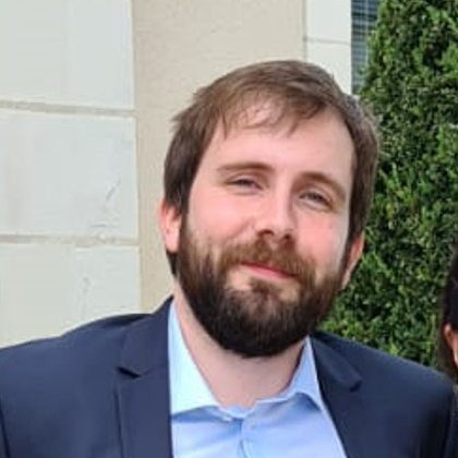 Homme souriant avec une barbe, vêtu d'un t-shirt noir, devant un fond blanc.
