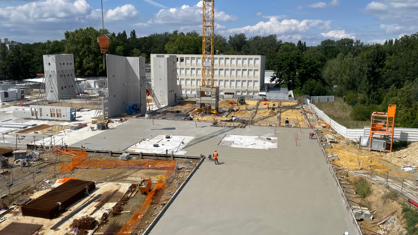 Chantier de construction avec murs en béton, grue et surfaces en béton fraîchement coulées.